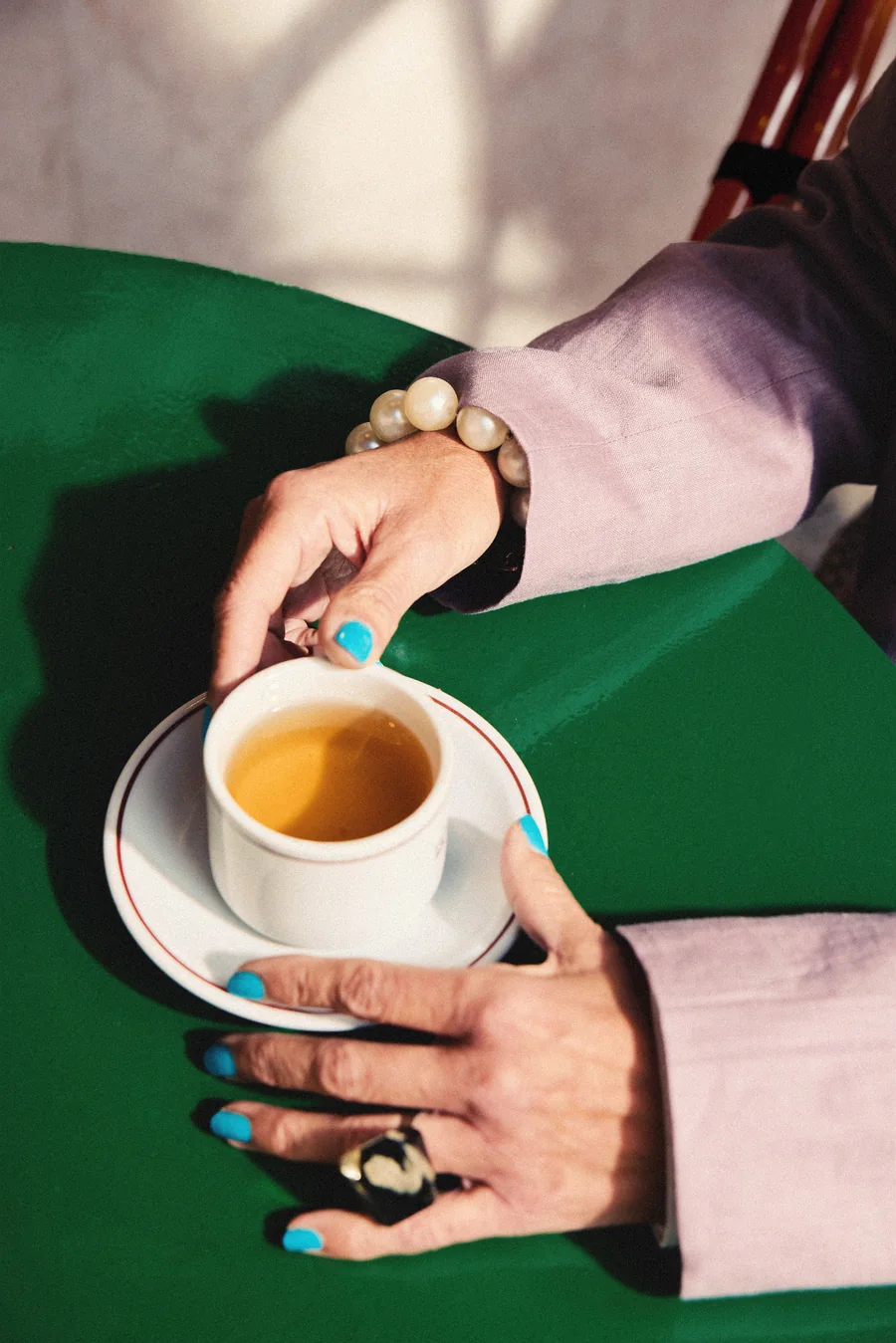 Hände reichen eine Tasse Espresso über einen grünen Tisch